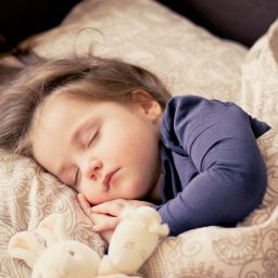 A female toddler sleeping in bed with a stuffed animal.