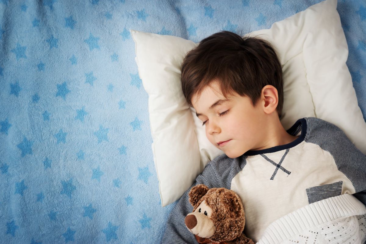 Child sleeping in bed with a teddy bear tucked under their arm