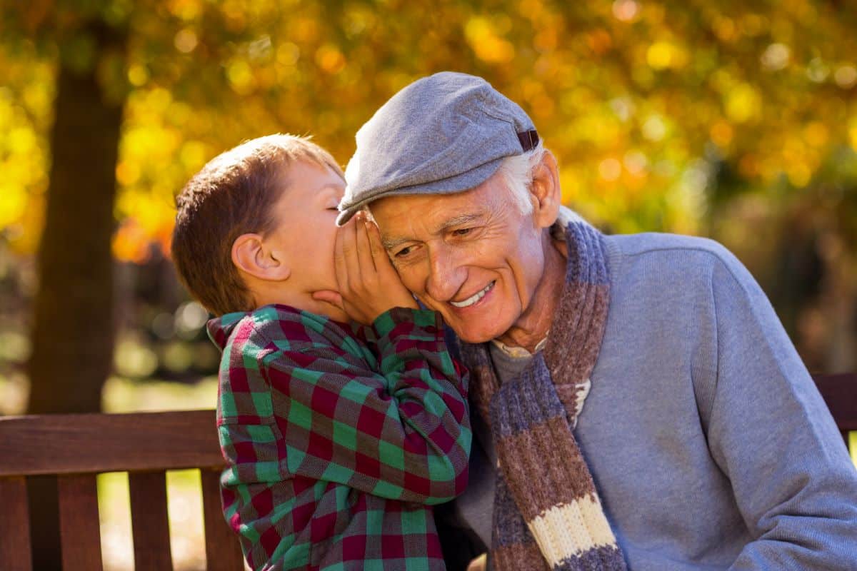 Child speaking into grandfathers ear as the grandfather smiles