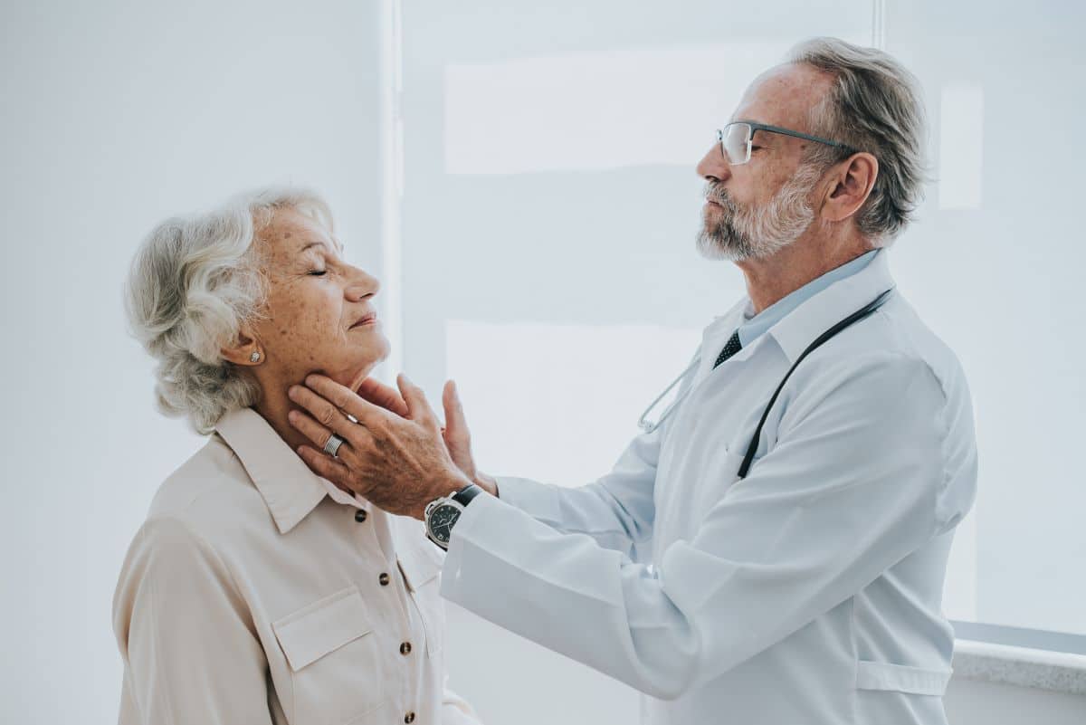 doctor in a medical setting is feeling an older patients throat for indications of tonsillitis